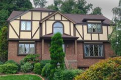 A large brick house with a brown roof is surrounded by trees.