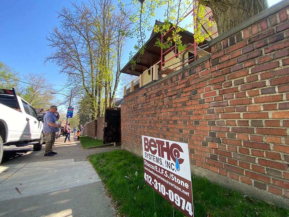 A man is standing next to a brick wall with a sign on it.