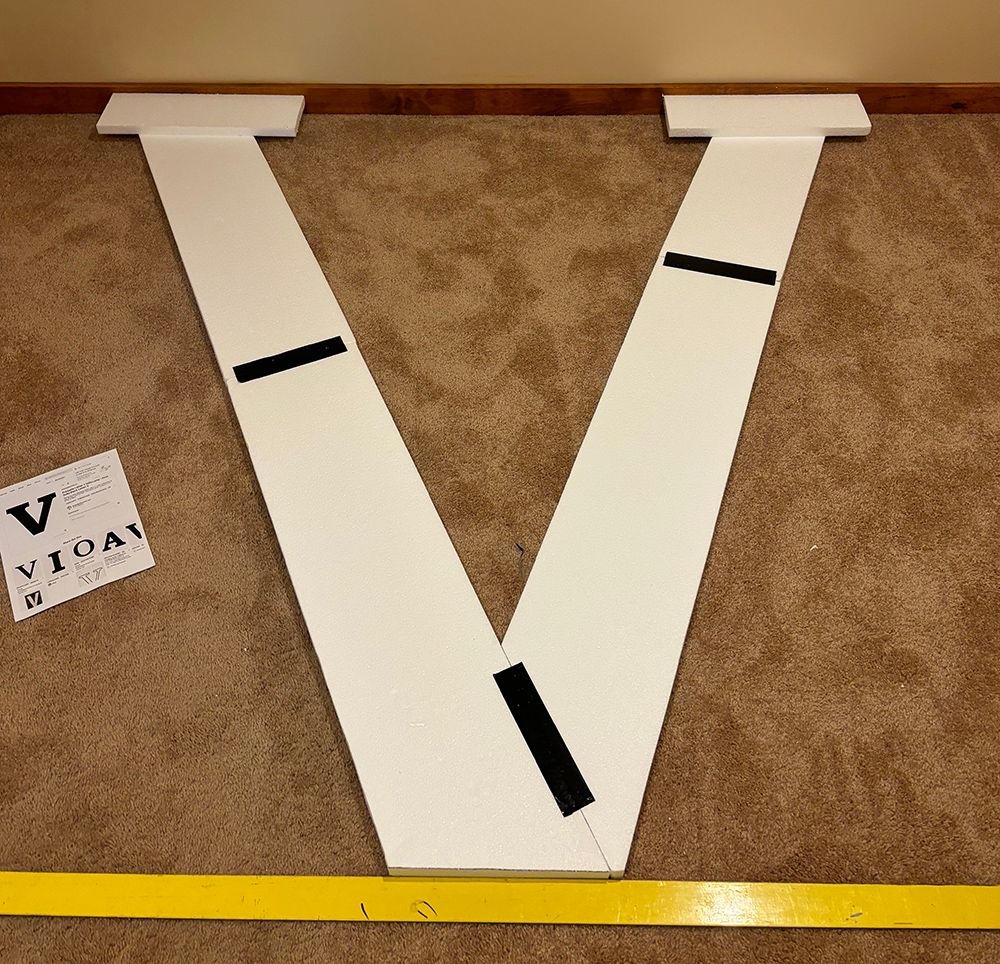 A large white letter v is sitting on a carpet next to a ruler