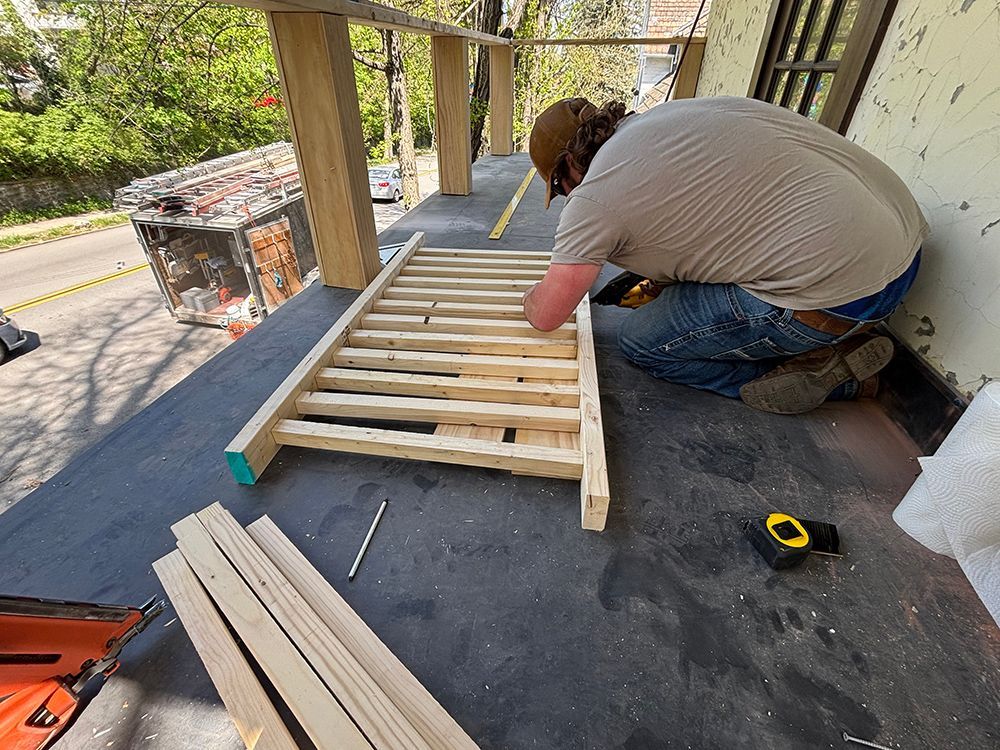 A man is measuring a piece of wood on a porch.