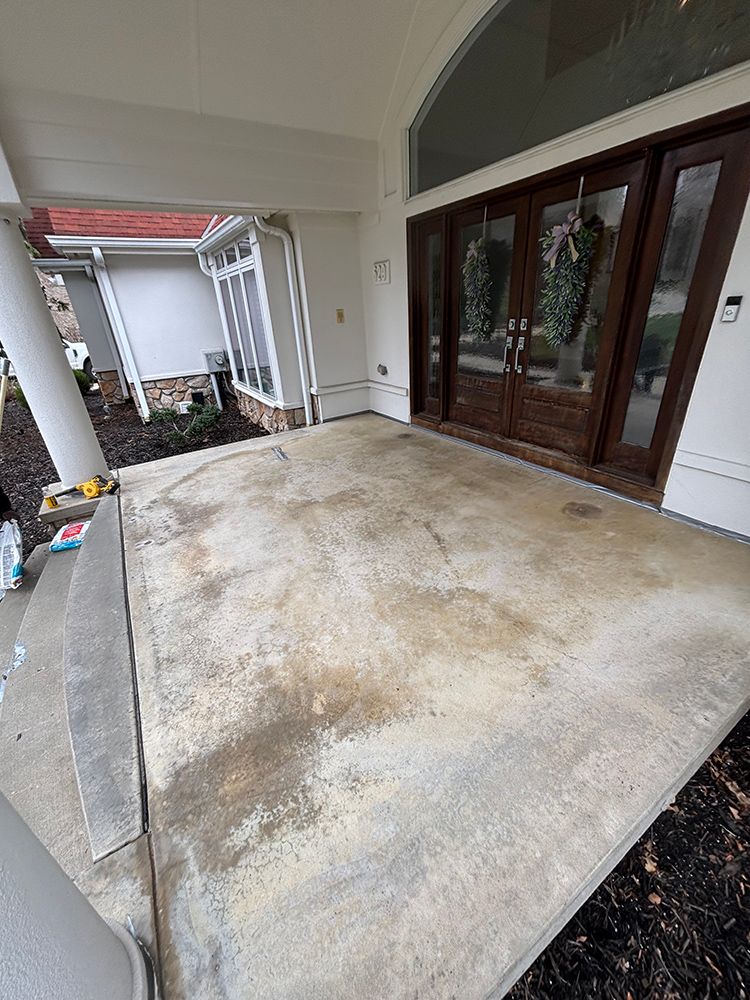 A concrete porch with a wooden door and a white house in the background.