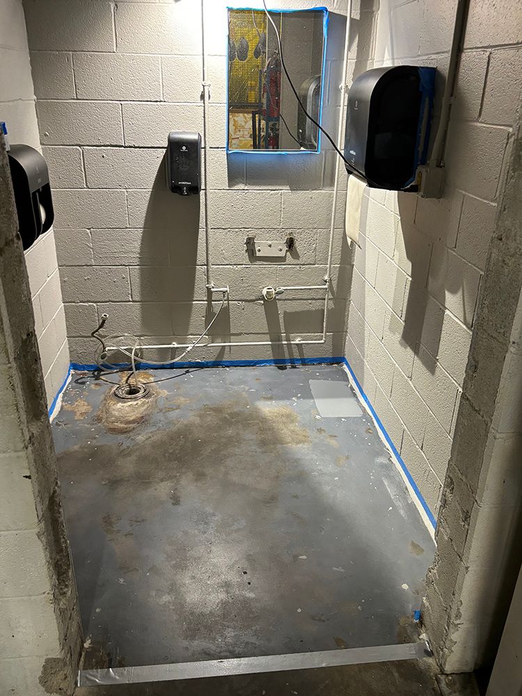 A bathroom with a concrete floor and a mirror on the wall.