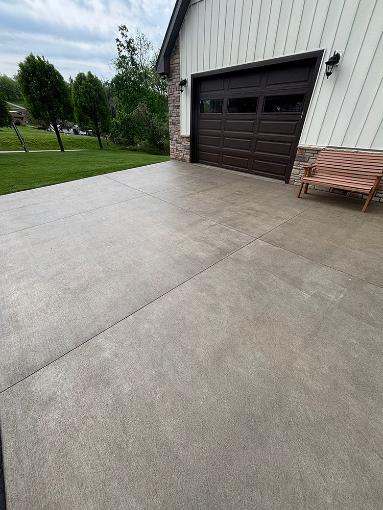A concrete driveway leading to a garage with a bench in front of it.