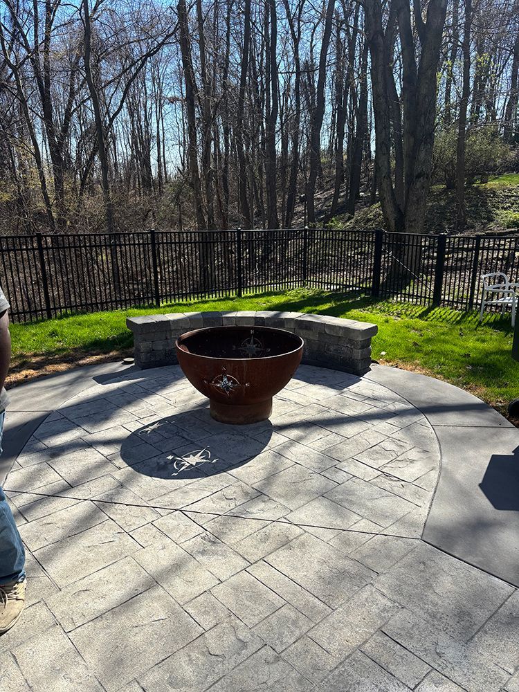 A fire pit is sitting on top of a patio next to a fence.