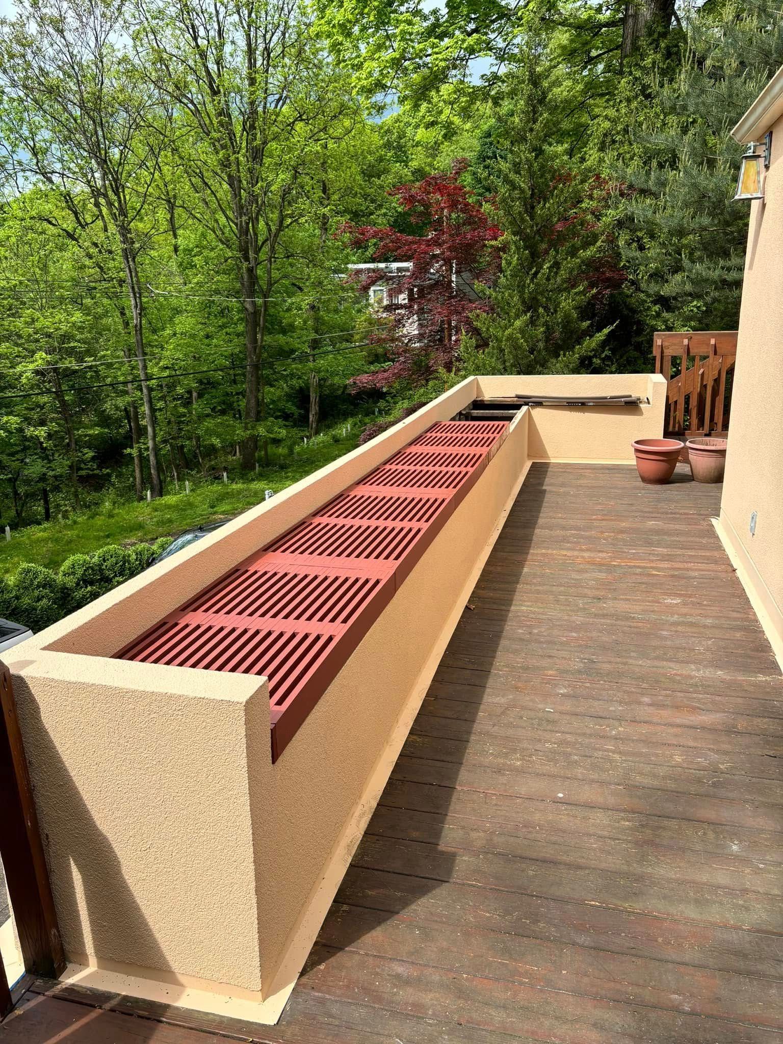 A wooden deck with a bench and trees in the background.