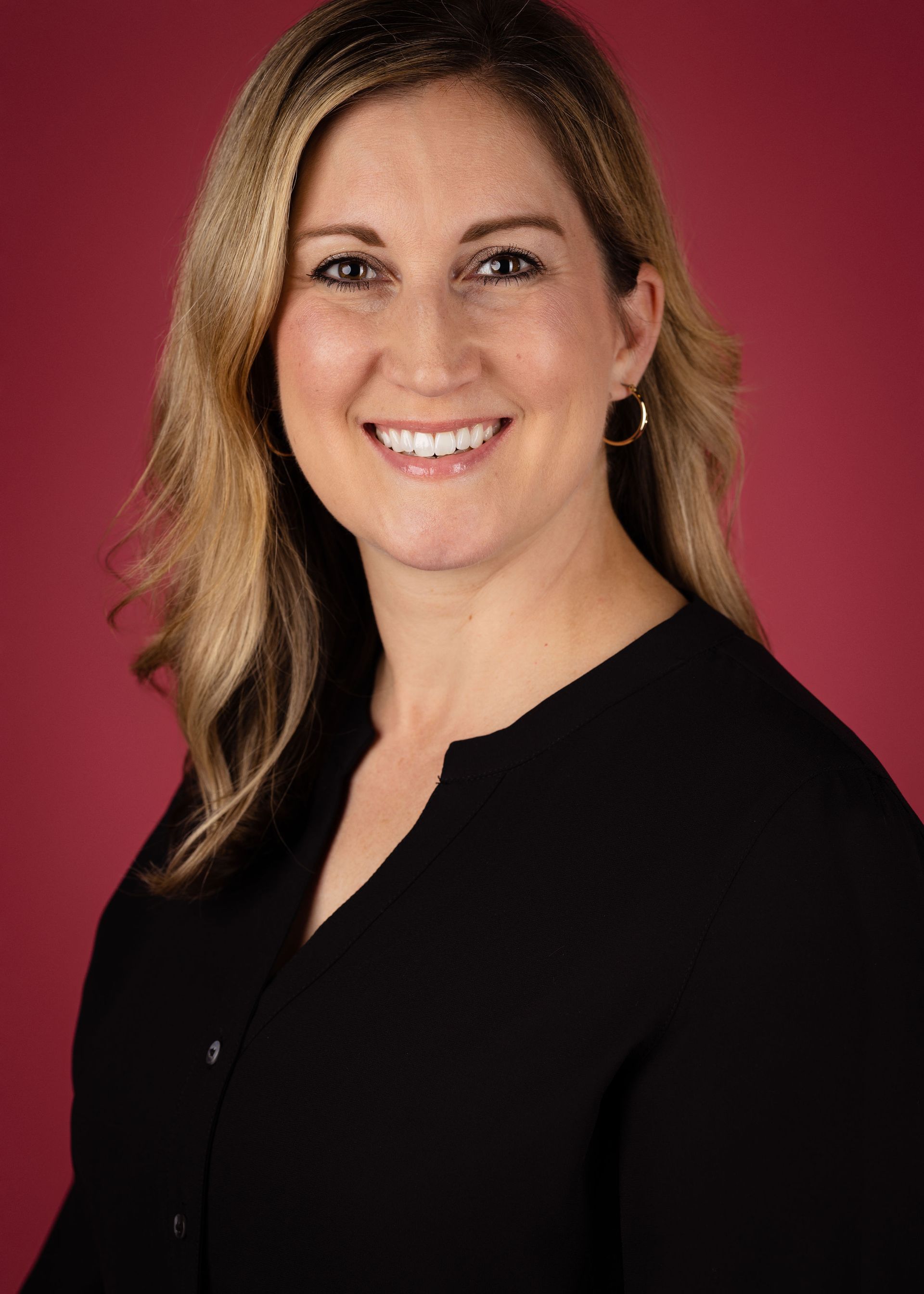 Kelly Van Buren, A woman in a black shirt is smiling in front of a red background.
