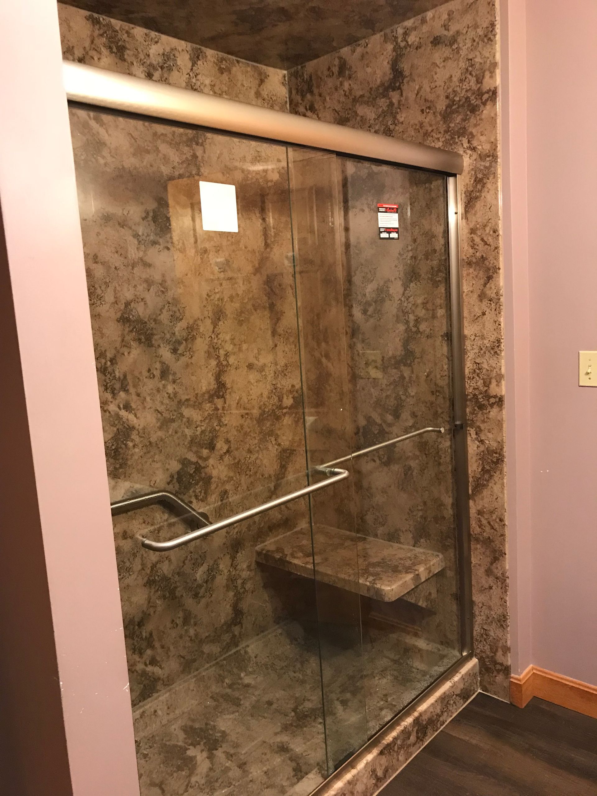 Shower with glass doors and a built-in seat, featuring brown marble-like tiles and silver fixtures.