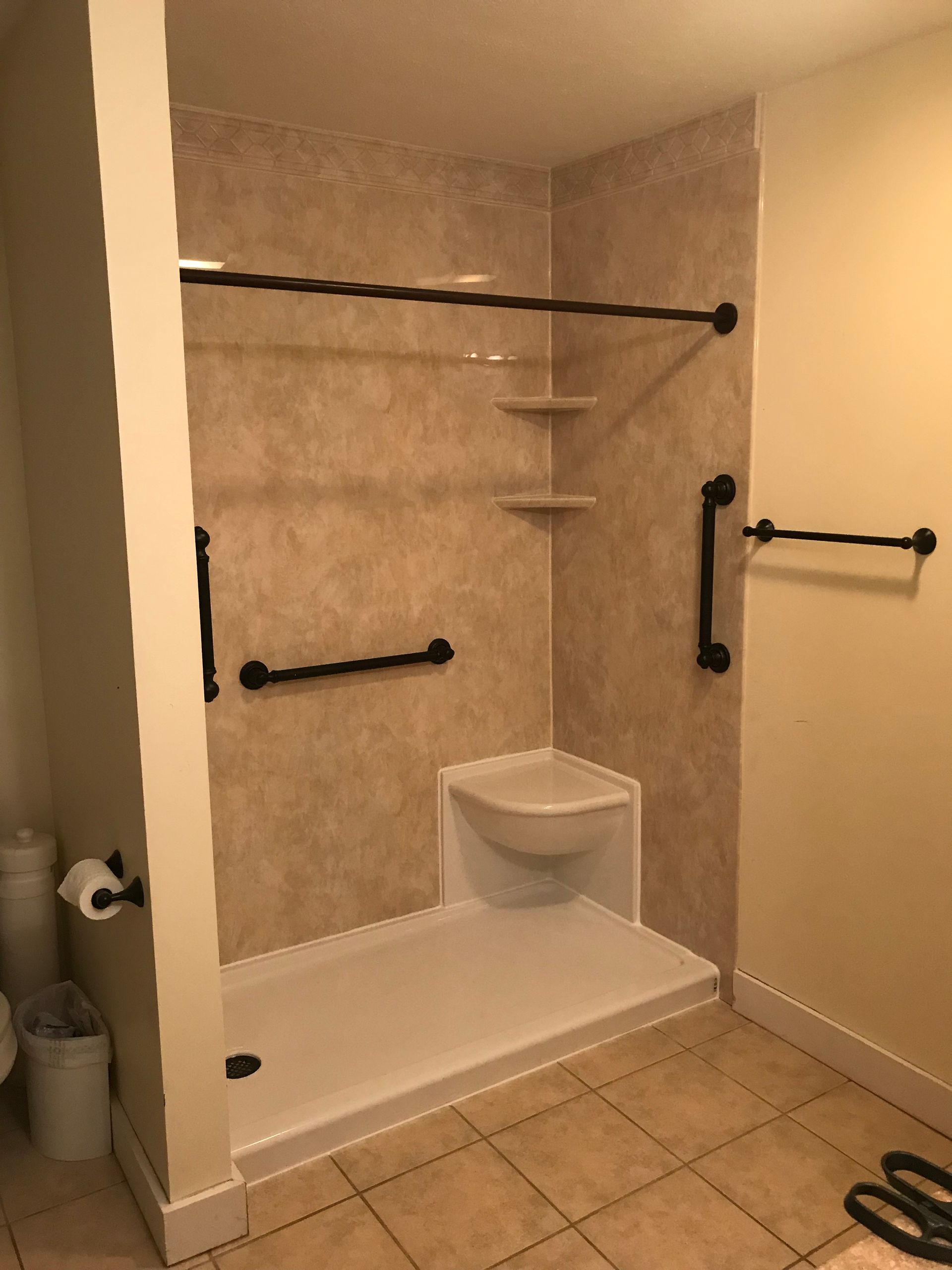 Accessible shower stall with grab bars, corner seat, neutral tones.