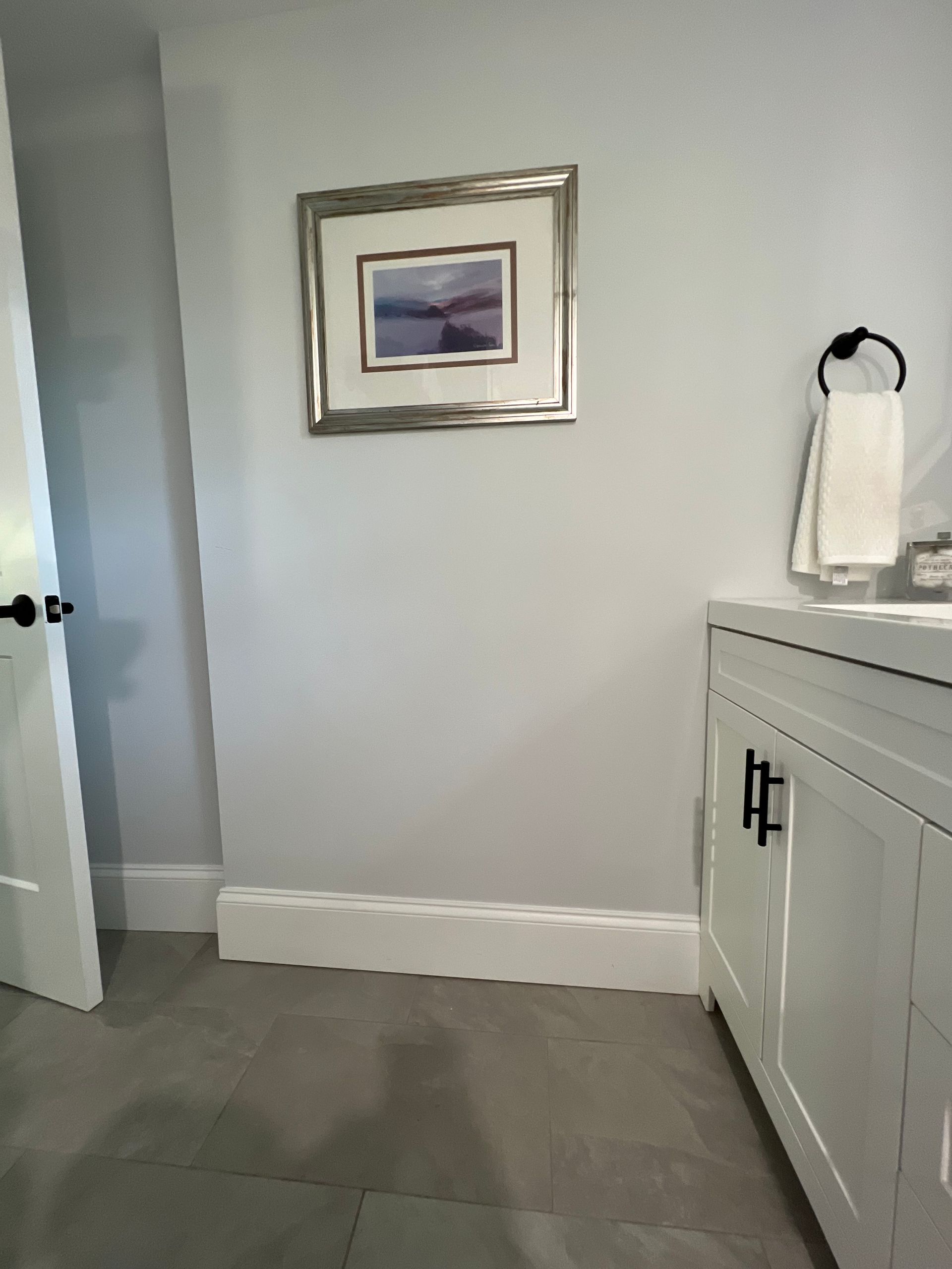 A bathroom with a white vanity and door, framed artwork, and gray walls and floor.