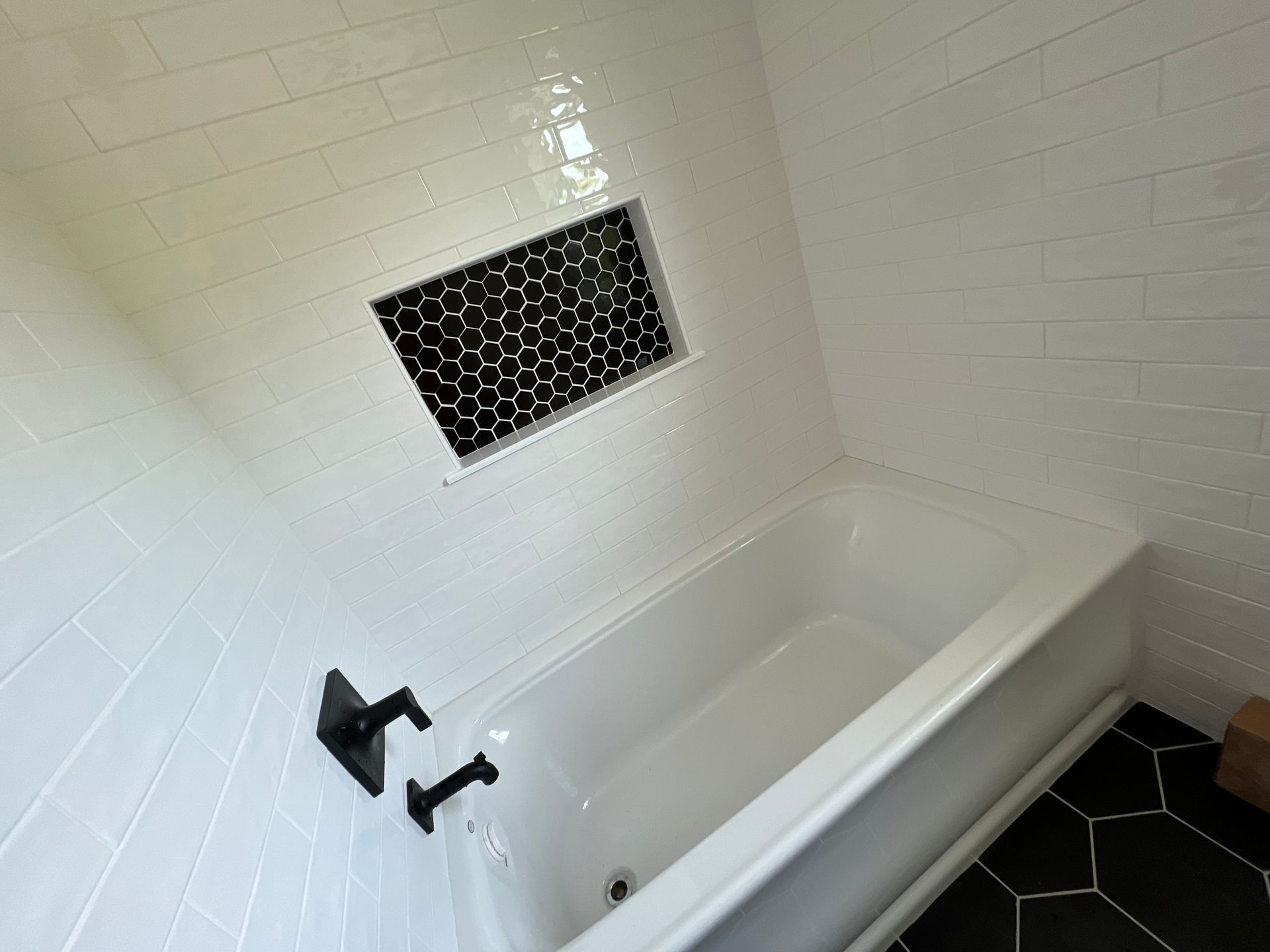 White tiled bathroom with black honeycomb-tiled alcove above a white bathtub, black faucet.