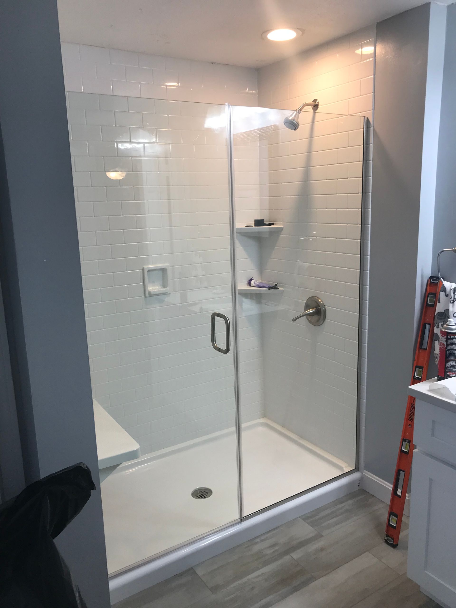 Shower stall with glass door, white walls, and gray tile floor.