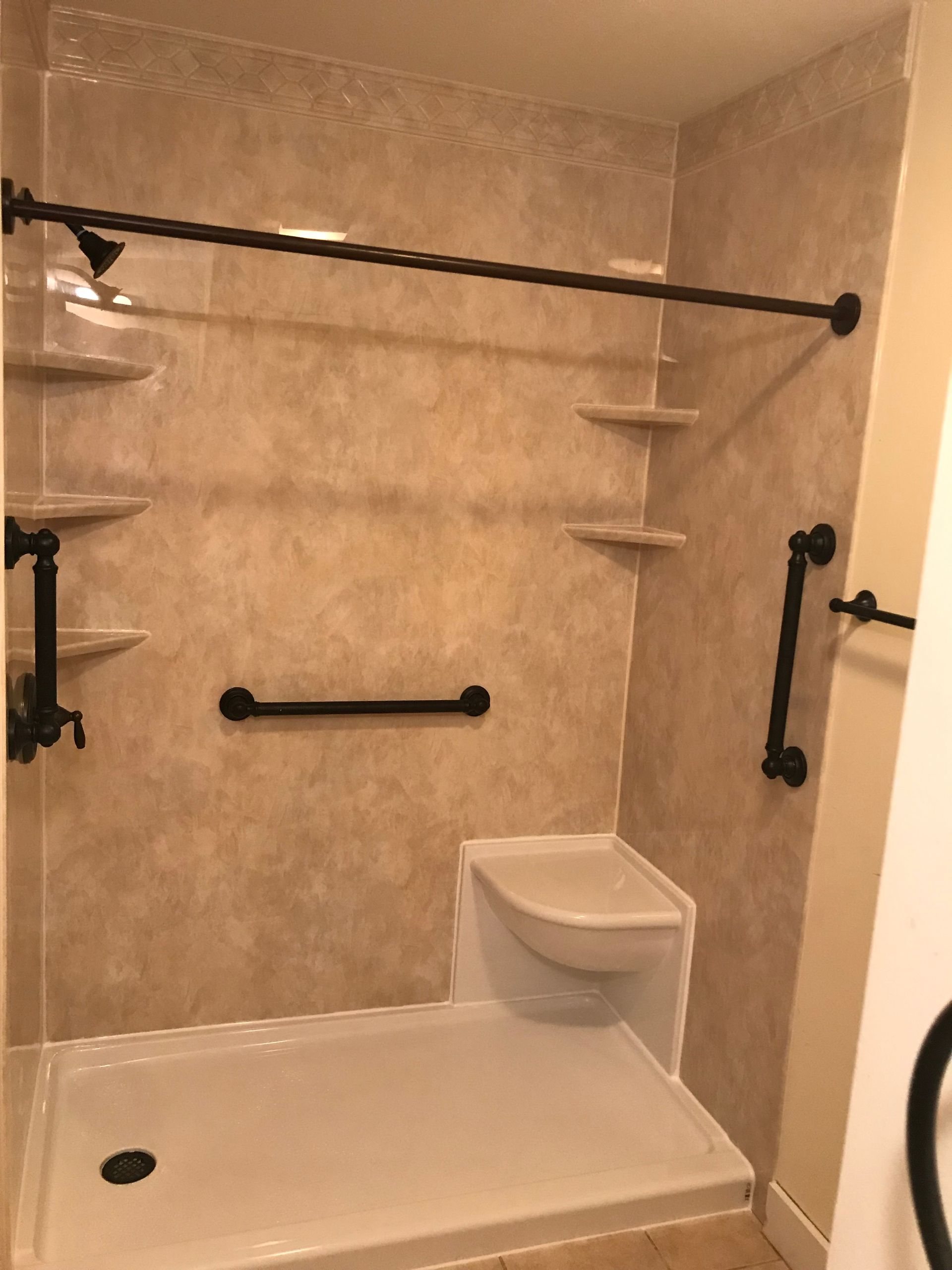 Accessible shower with grab bars and built-in shelves. Tan walls, white shower base, black fixtures.