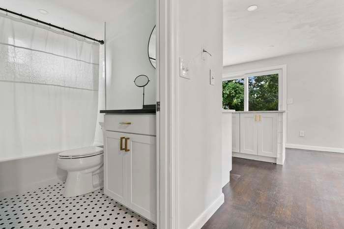 Bathroom and adjacent room. White cabinets with gold hardware, black countertops, and hexagonal floor tile.