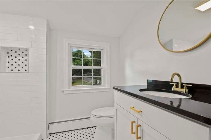 White bathroom with black countertop, gold accents, and window overlooking trees.