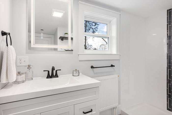 White bathroom with a vanity, mirror, window, and black accents.