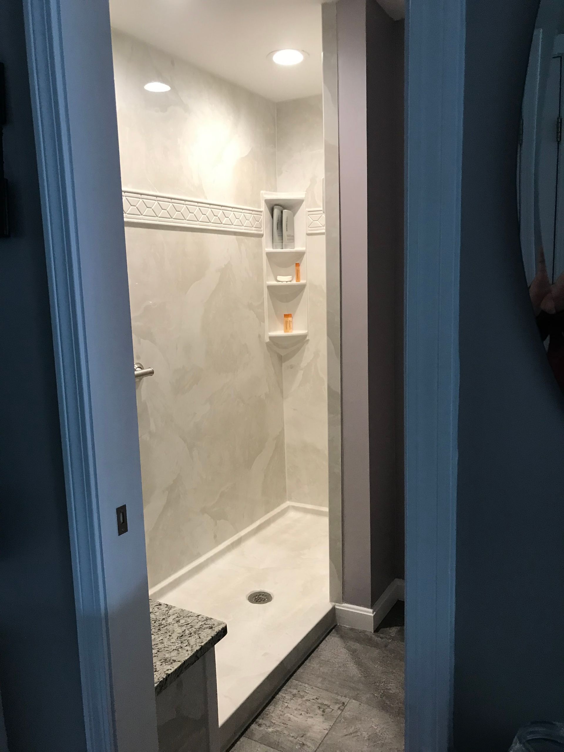 Shower stall with three built-in shelves. Beige tile walls with a decorative trim and recessed lighting.