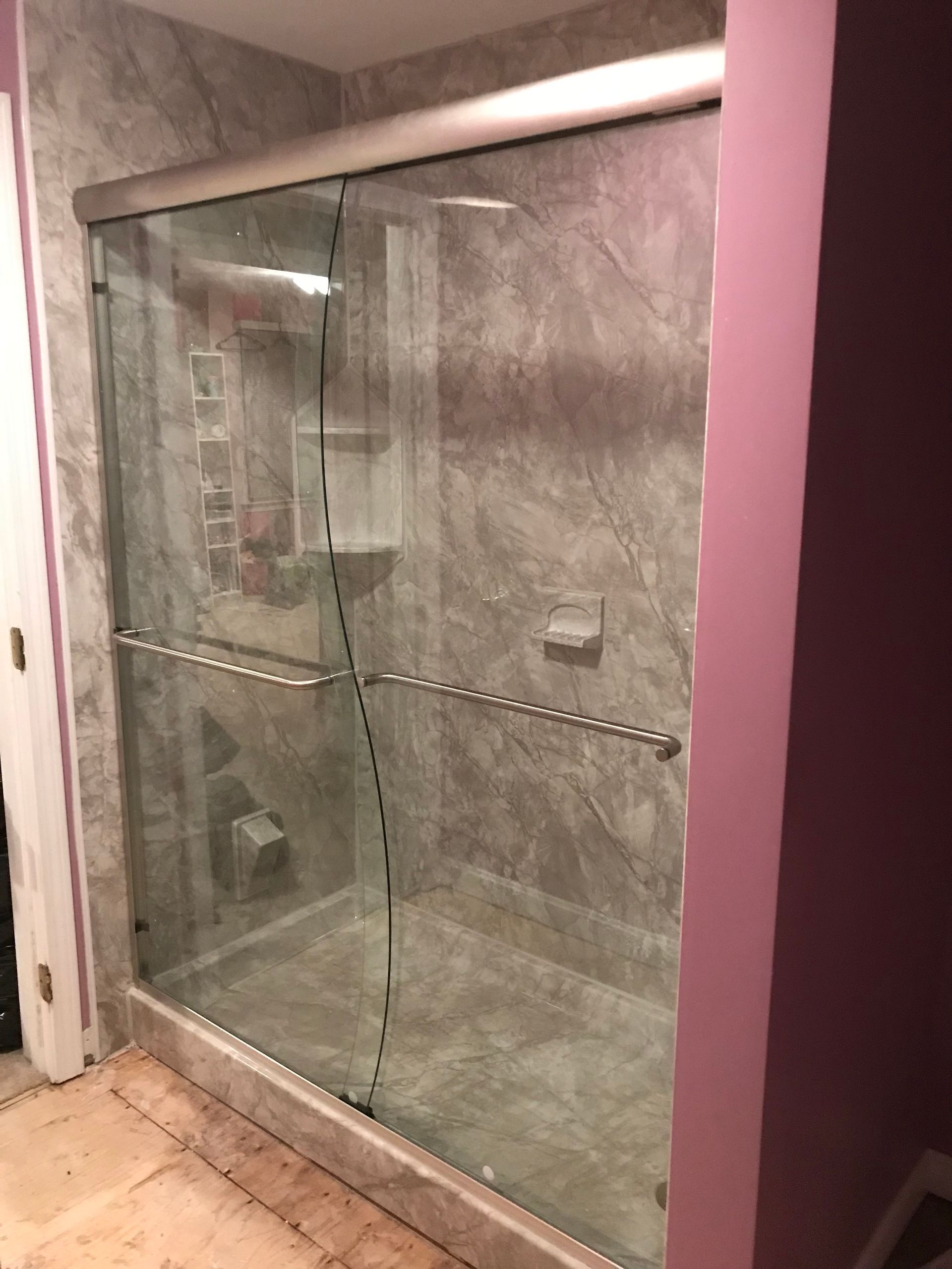 Glass shower enclosure with gray marble-look tile, silver fixtures, and a pink wall.