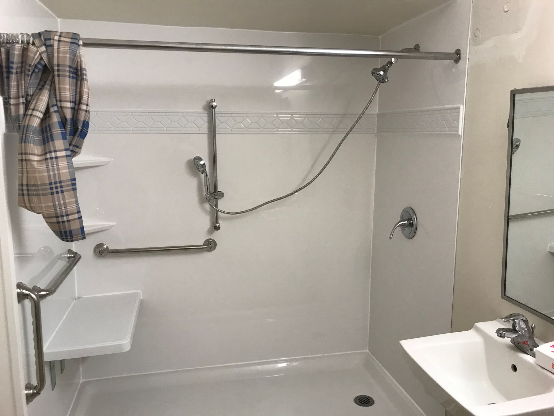 Accessible white shower with grab bars and a handheld showerhead. A sink and mirror are visible.