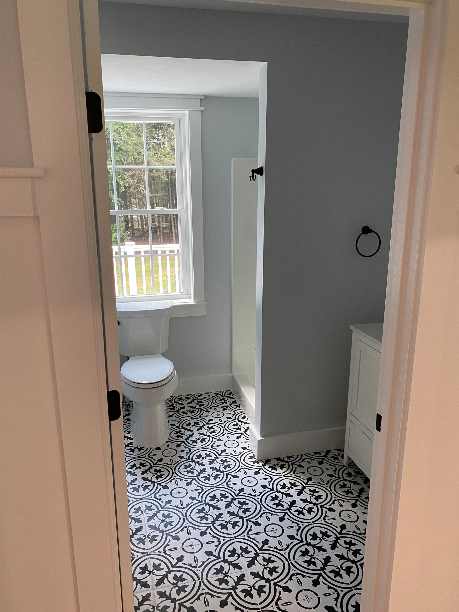Bathroom with patterned black and white floor, blue walls, white fixtures, and a window.