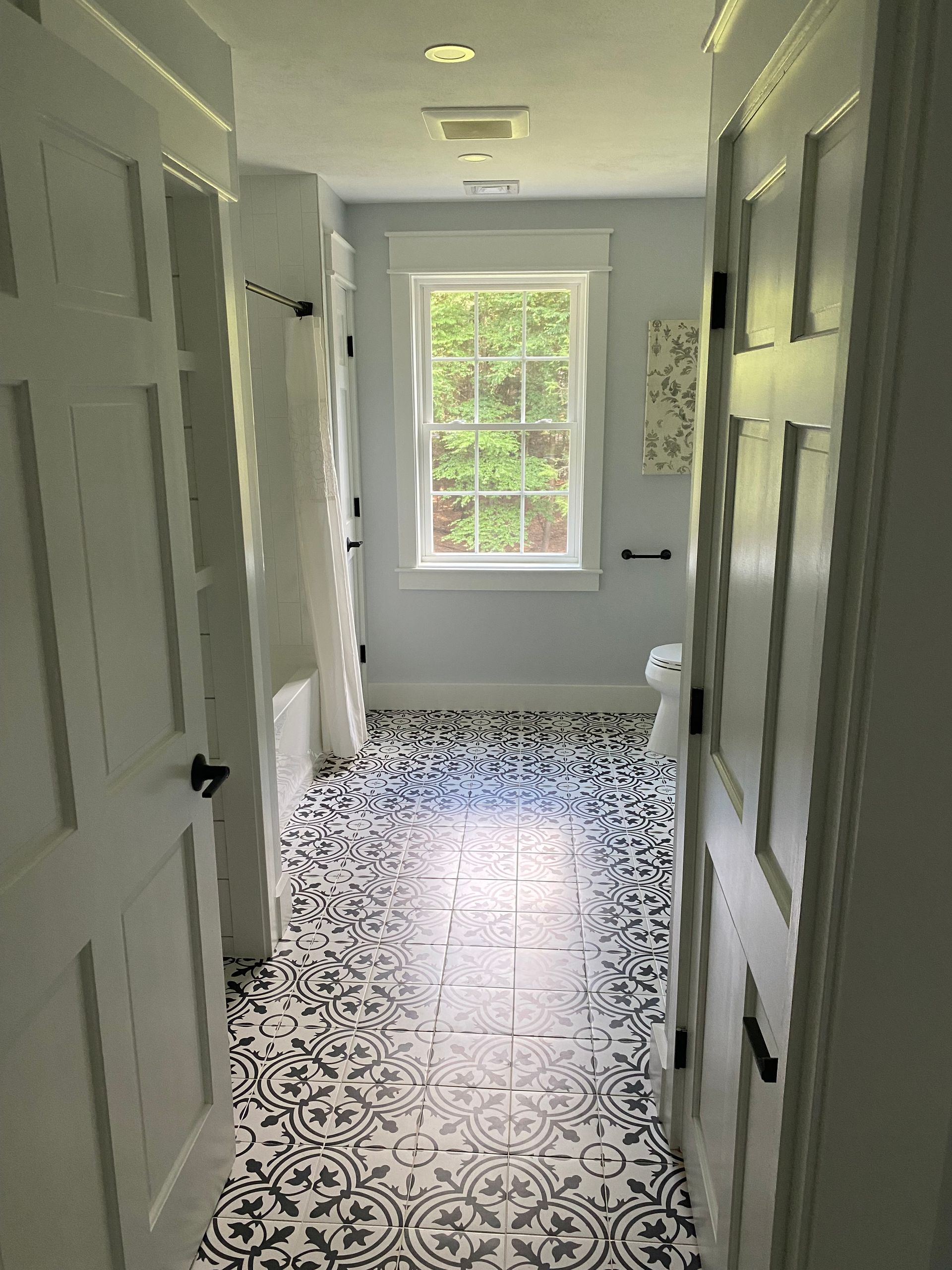 Bathroom hallway with patterned black and white floor tiles, a window, and white doors.