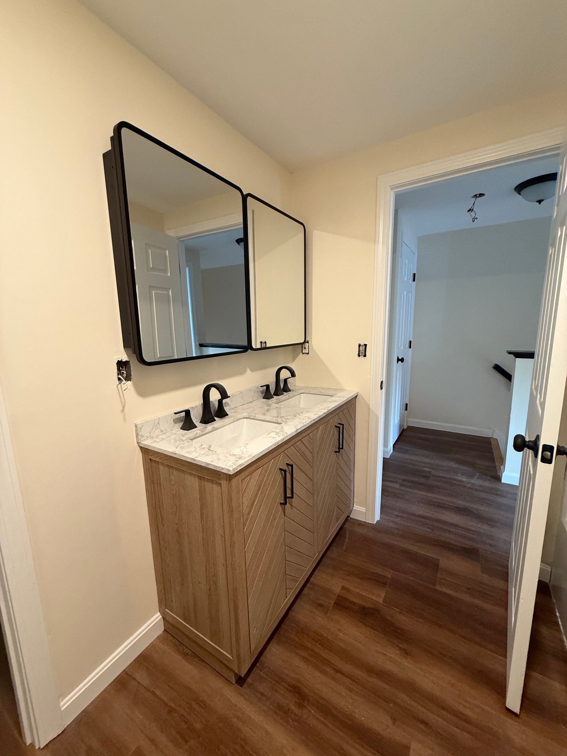 Bathroom with double vanity, two black-framed mirrors, and wooden cabinetry. The room has hardwood floors.