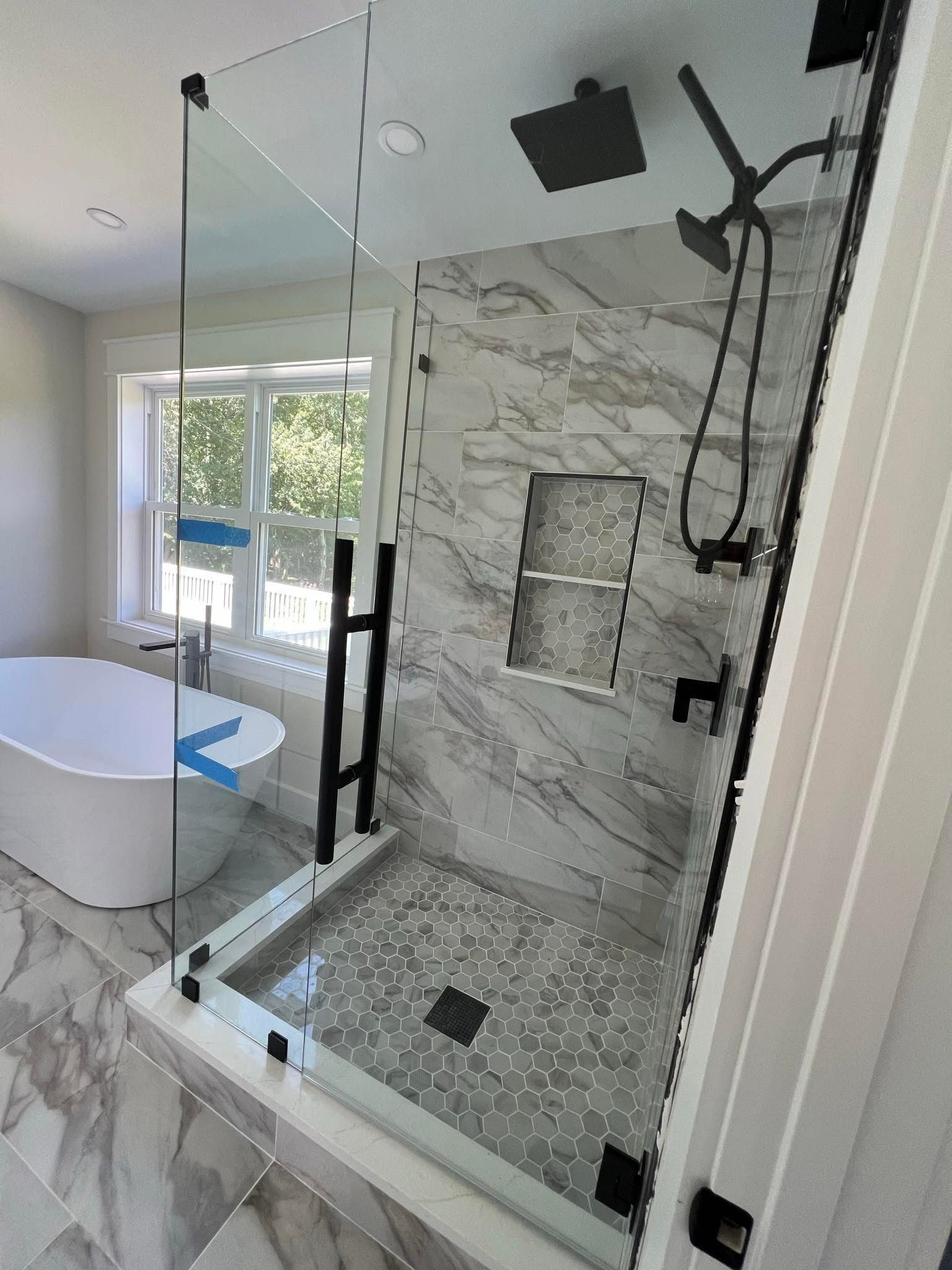 Modern bathroom with glass shower, marble tile, black fixtures, and a freestanding tub.
