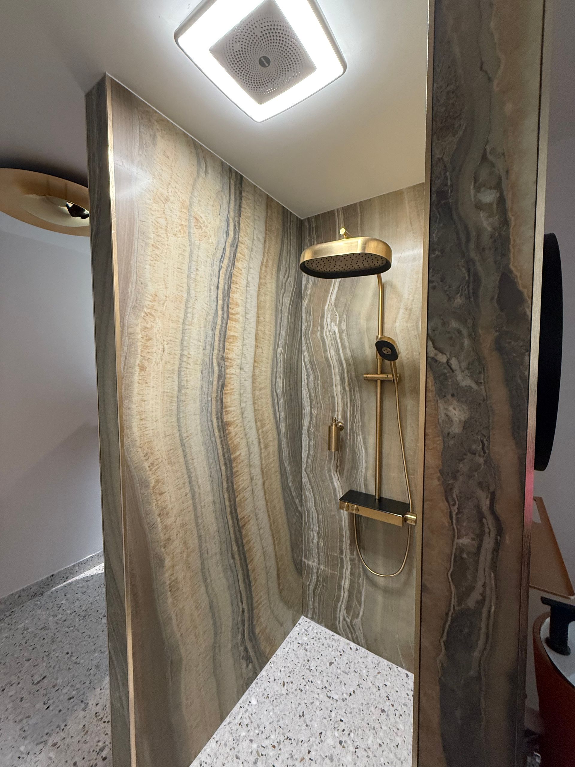 Shower stall with gold fixtures and striped brown and beige stone-like walls.