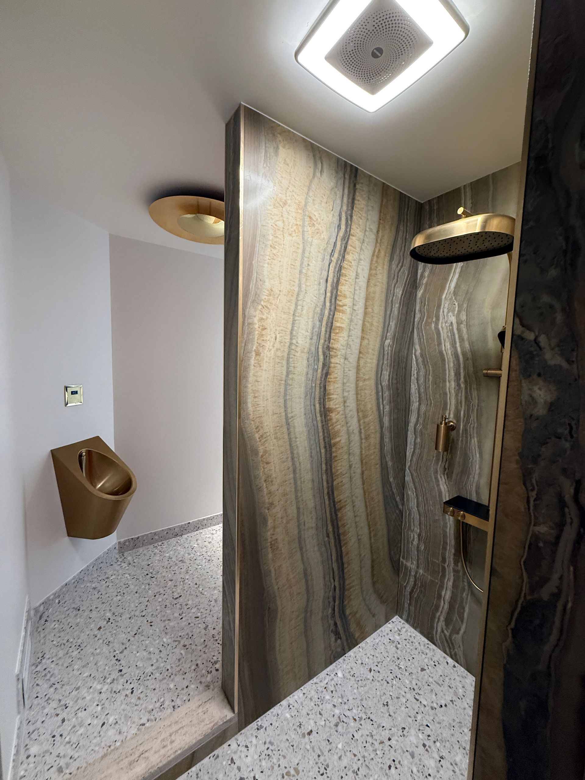 Luxurious bathroom: gold fixtures, marbled shower, terrazzo floor, modern lighting.