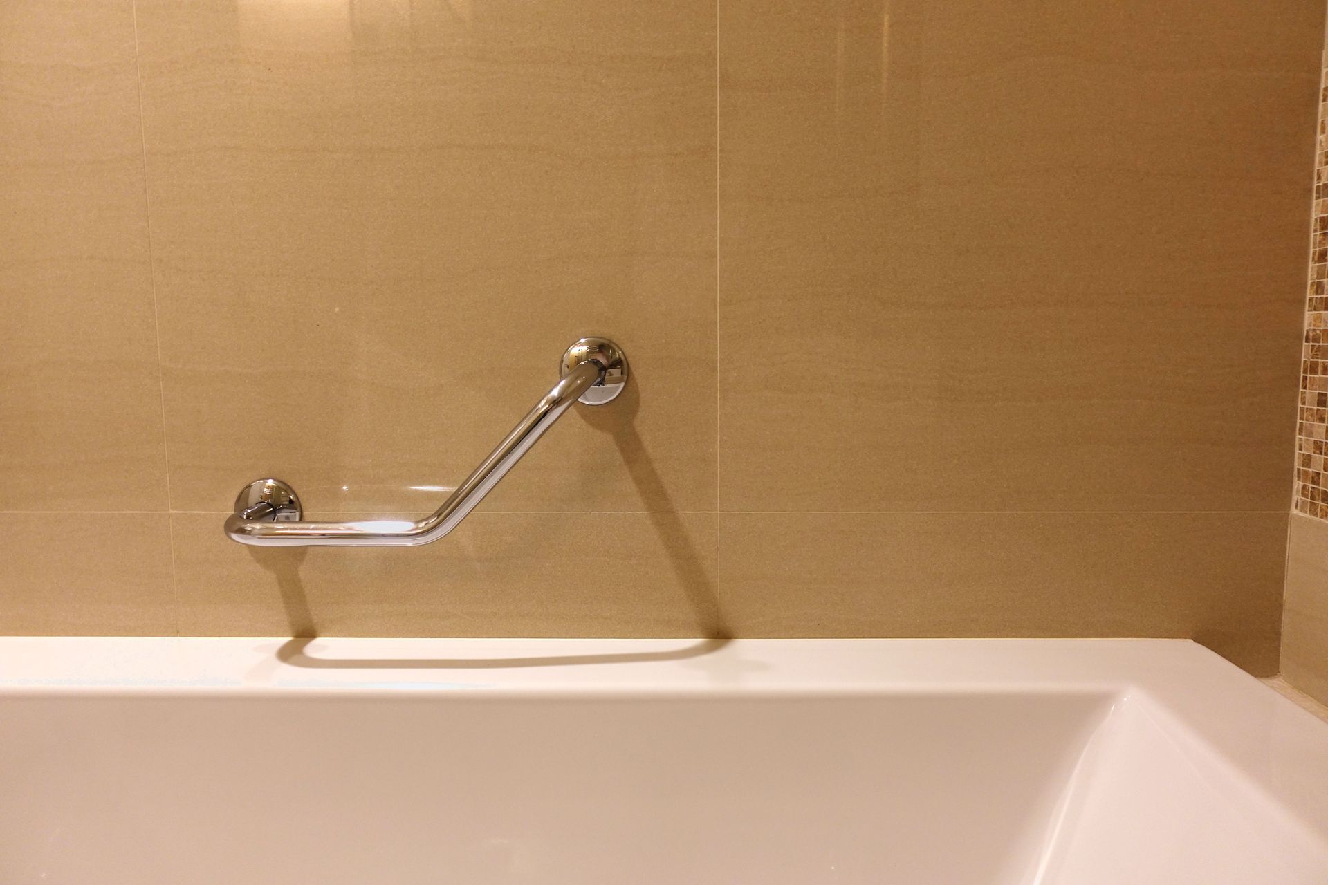 Chrome grab bar mounted on a beige tile wall above a white bathtub.