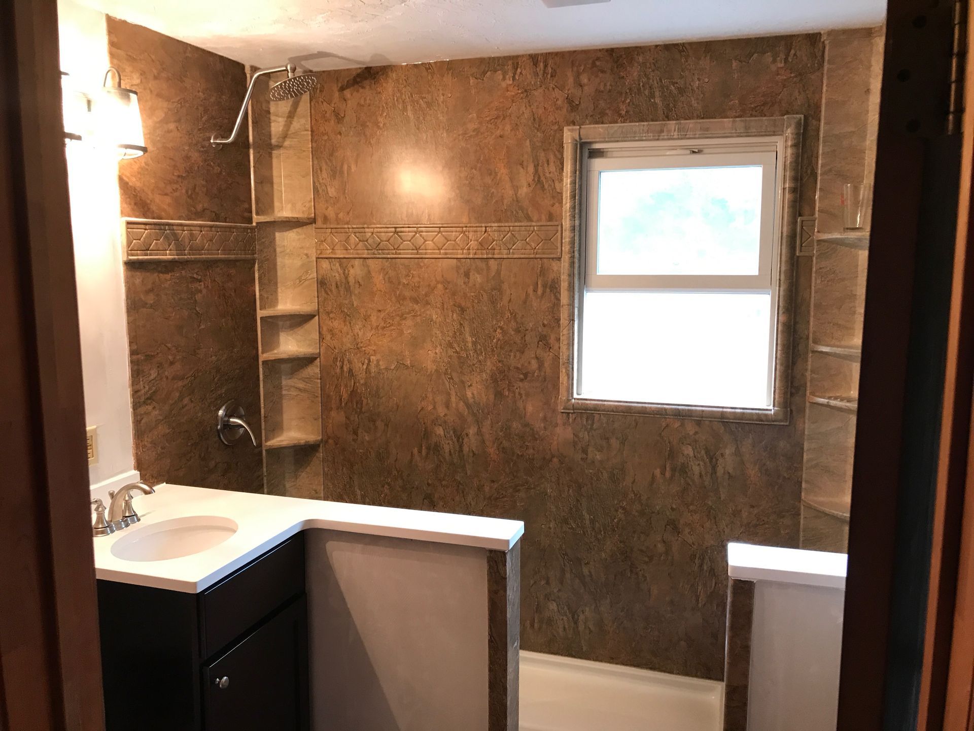 Bathroom with brown textured walls, white sink, dark cabinet, and window.