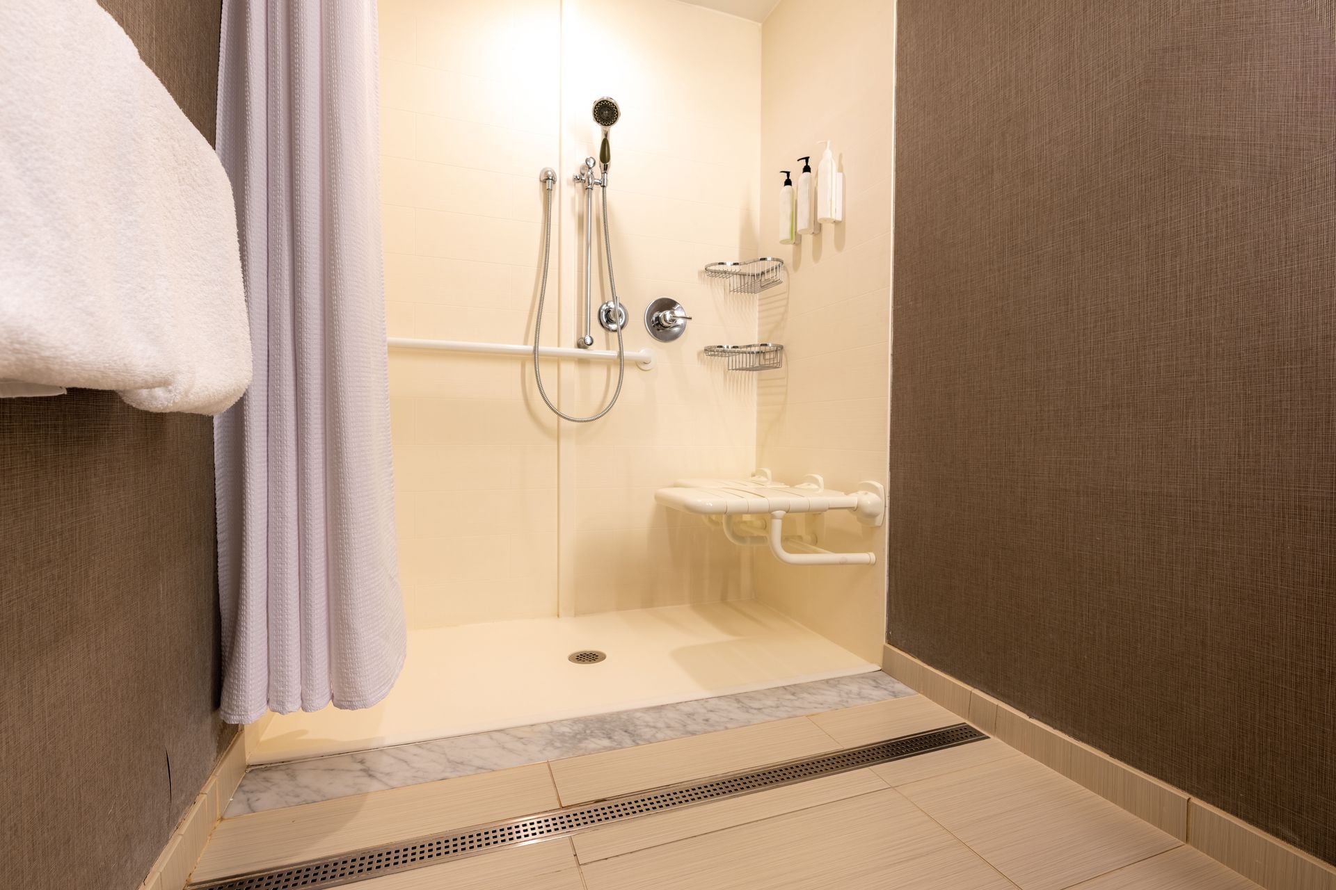 Accessible hotel shower with grab bars, shower seat, and handheld showerhead.