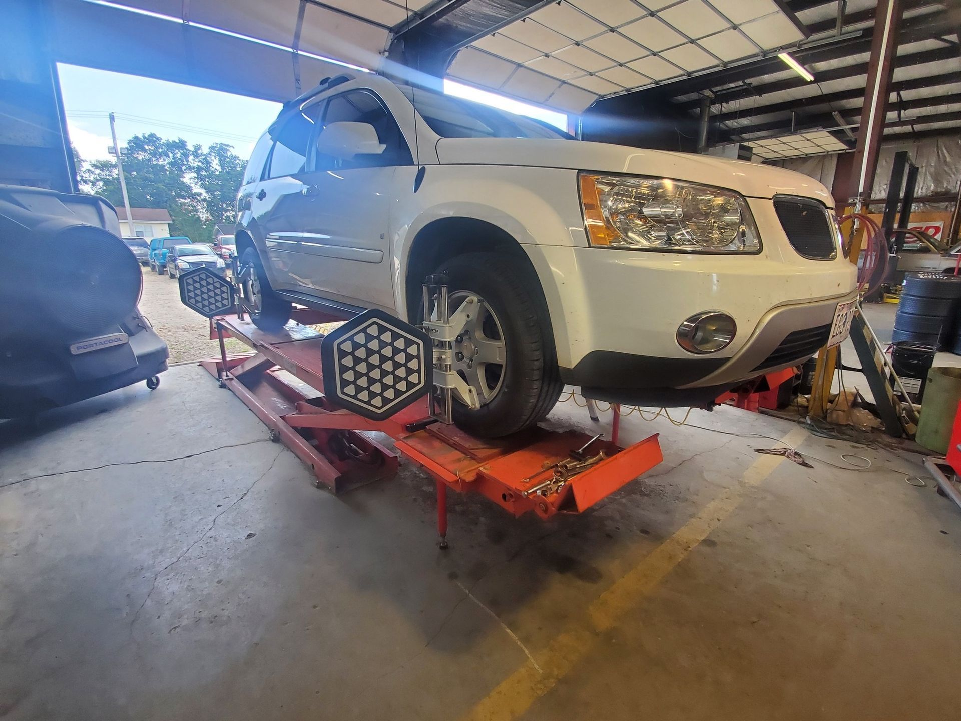 White SUV on a red lift in a garage, undergoing a wheel alignment.
