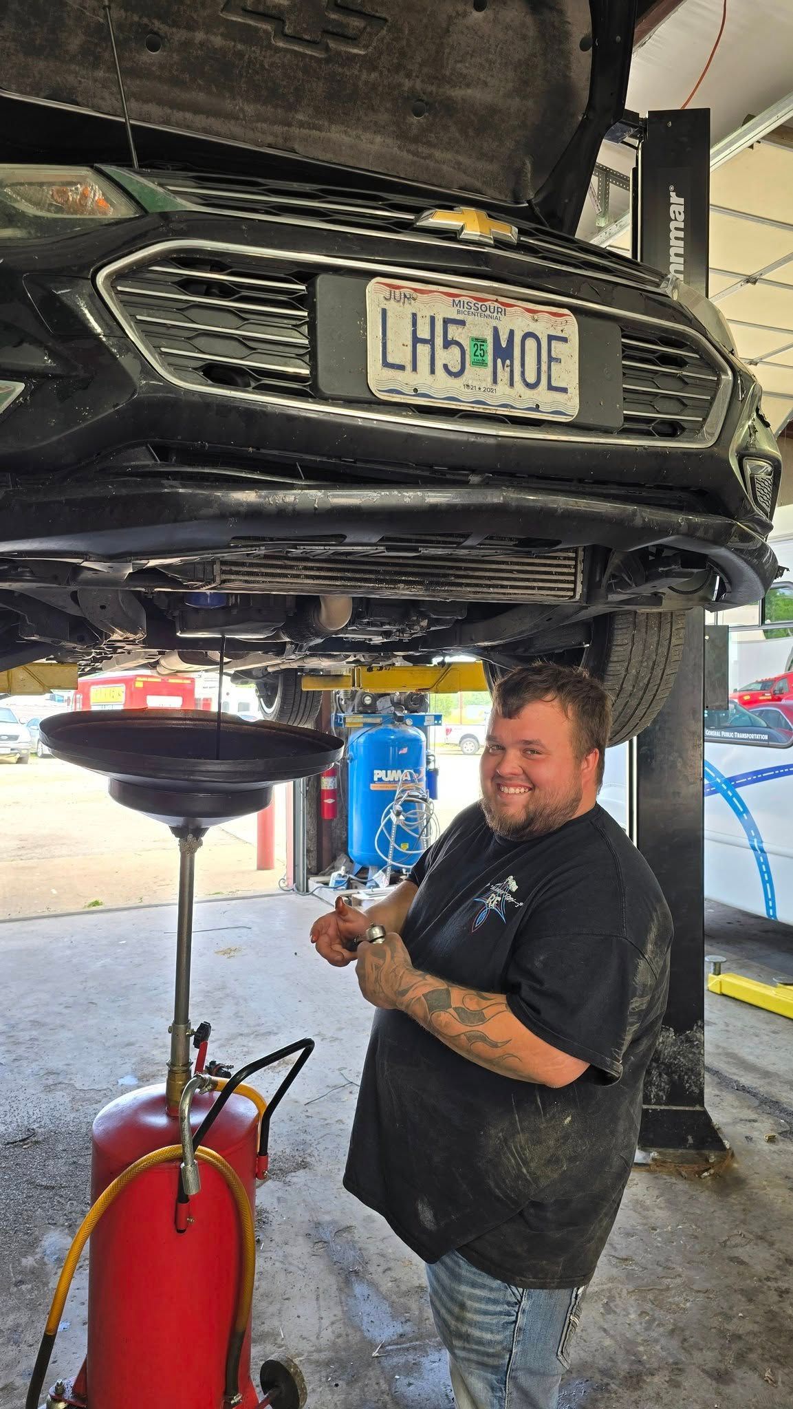 Man smiling under a car on a lift in a repair shop. Oil drain in use.