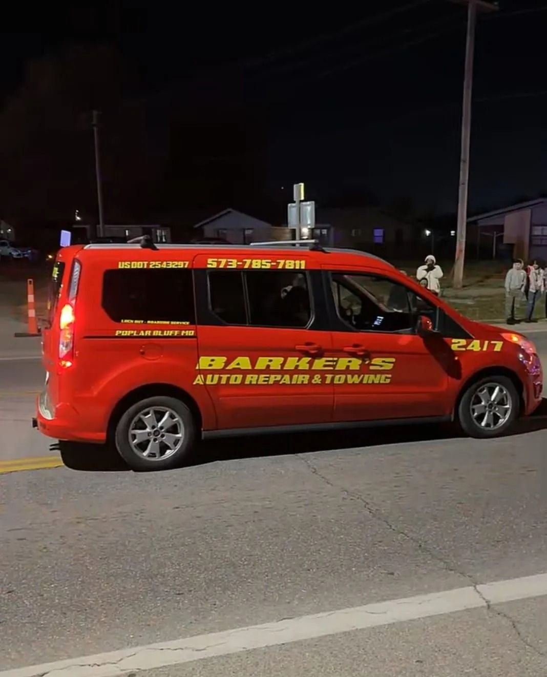 Red Barker's Auto Repair & Towing van parked on a dark street with emergency cones and people nearby.