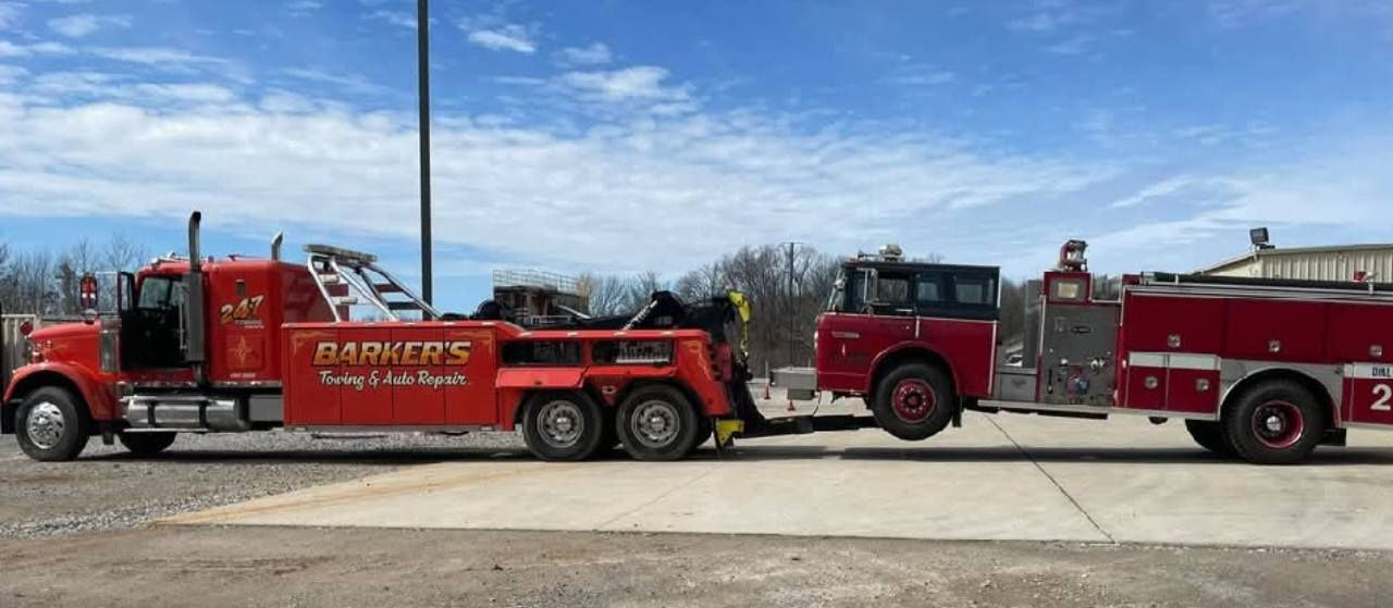 A red tow truck hauling an old red fire truck on a sunny day.