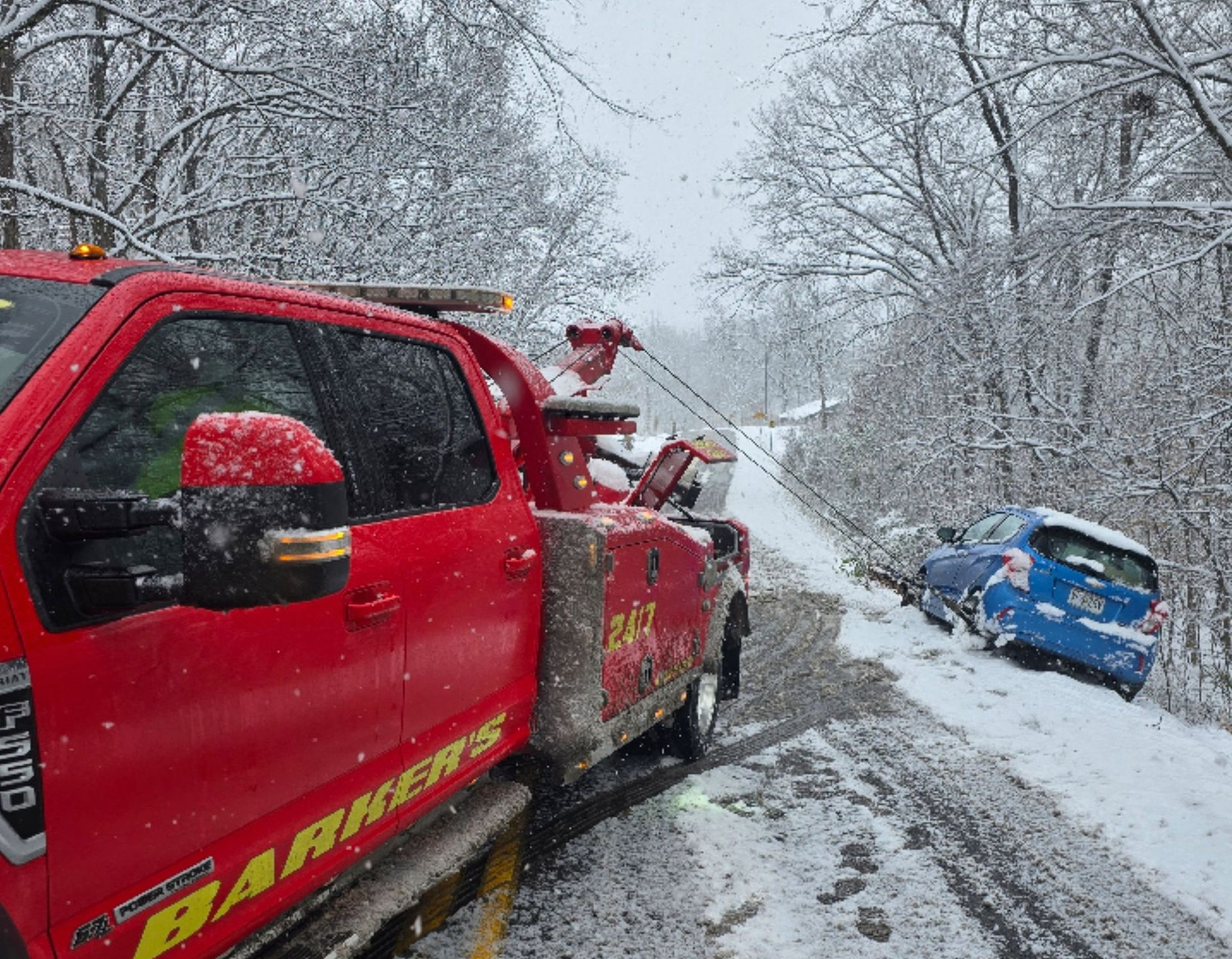 Red tow truck assisting a blue car that slid off a snowy road.
