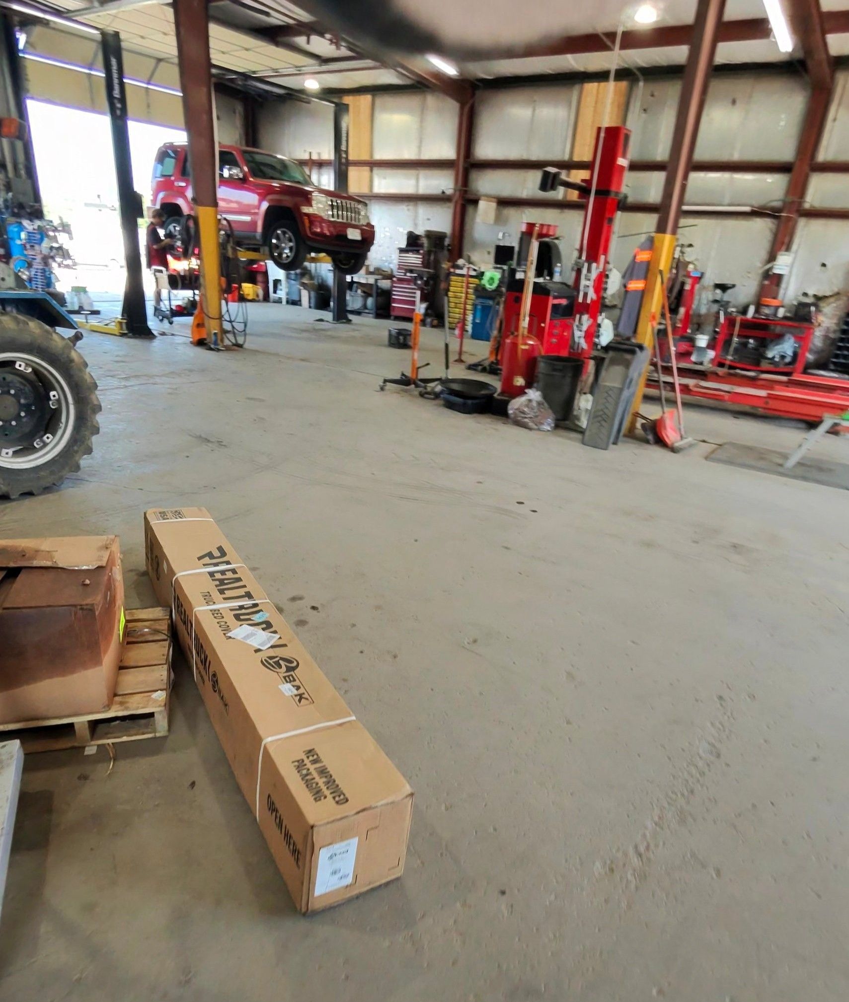 A car repair shop with a vehicle on a lift, boxes on the floor, and various tools.