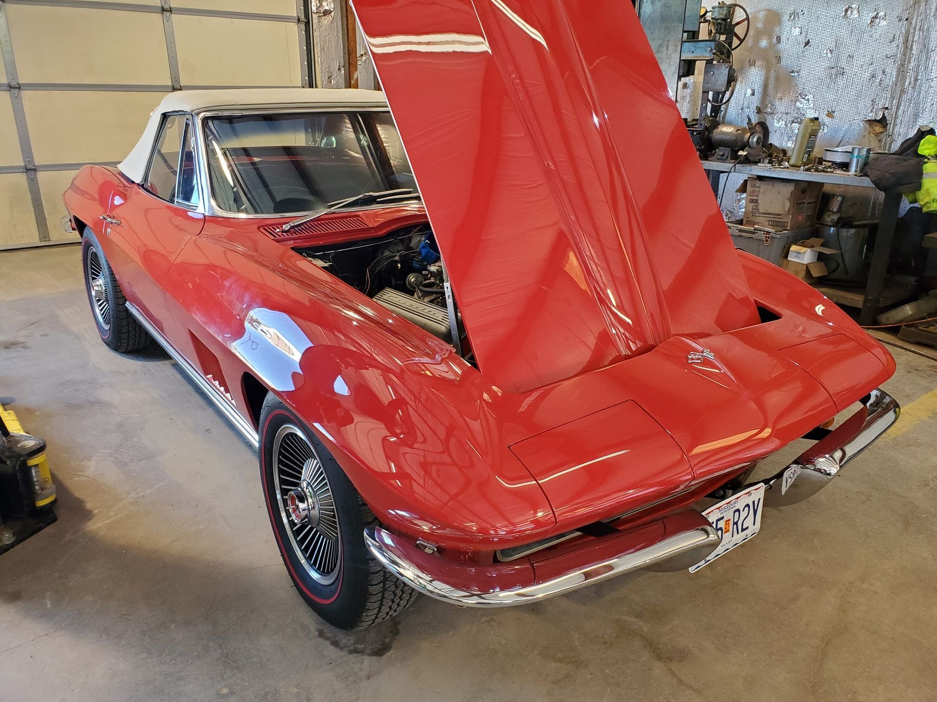 Red convertible Corvette with its hood open, in a garage.