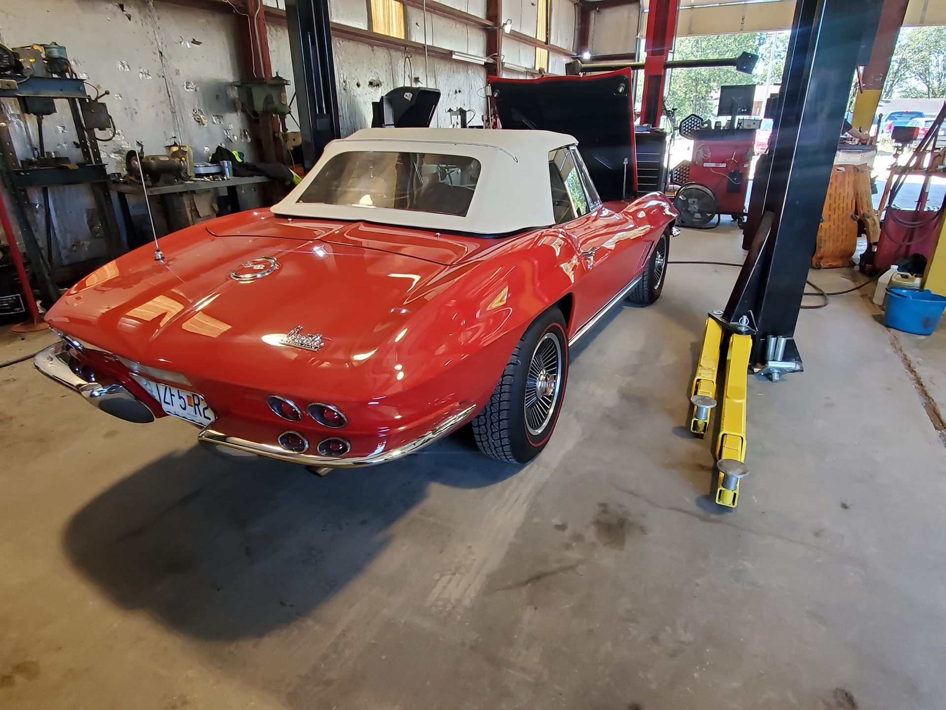 Red convertible Corvette in a garage, white soft top, chrome details.