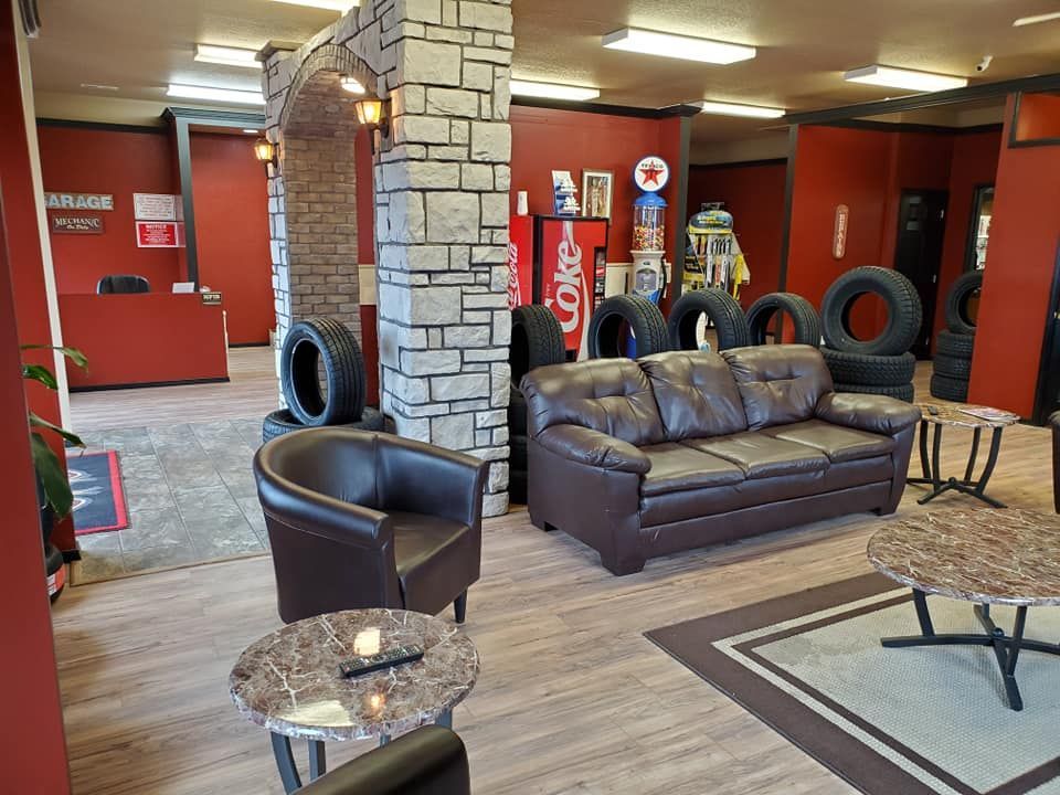 Tire shop waiting area with leather furniture, a faux stone pillar, and tires.