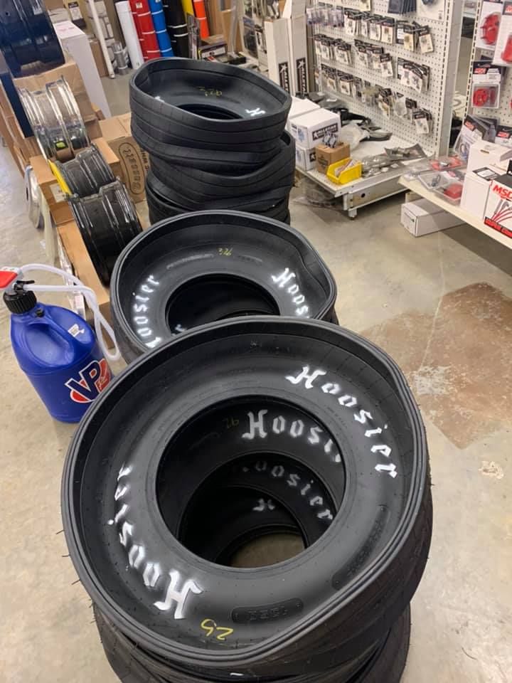 Stacks of Hoosier racing tires inside a shop, with a blue VP Racing fuel jug visible.