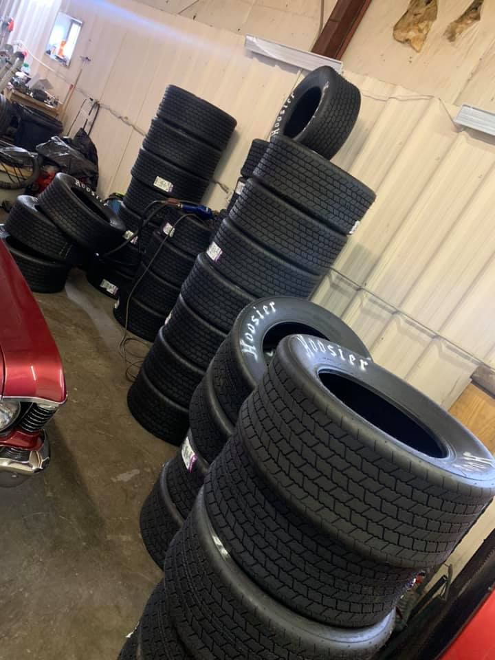 Stacks of Hoosier racing tires inside a garage. Some tires have white lettering.