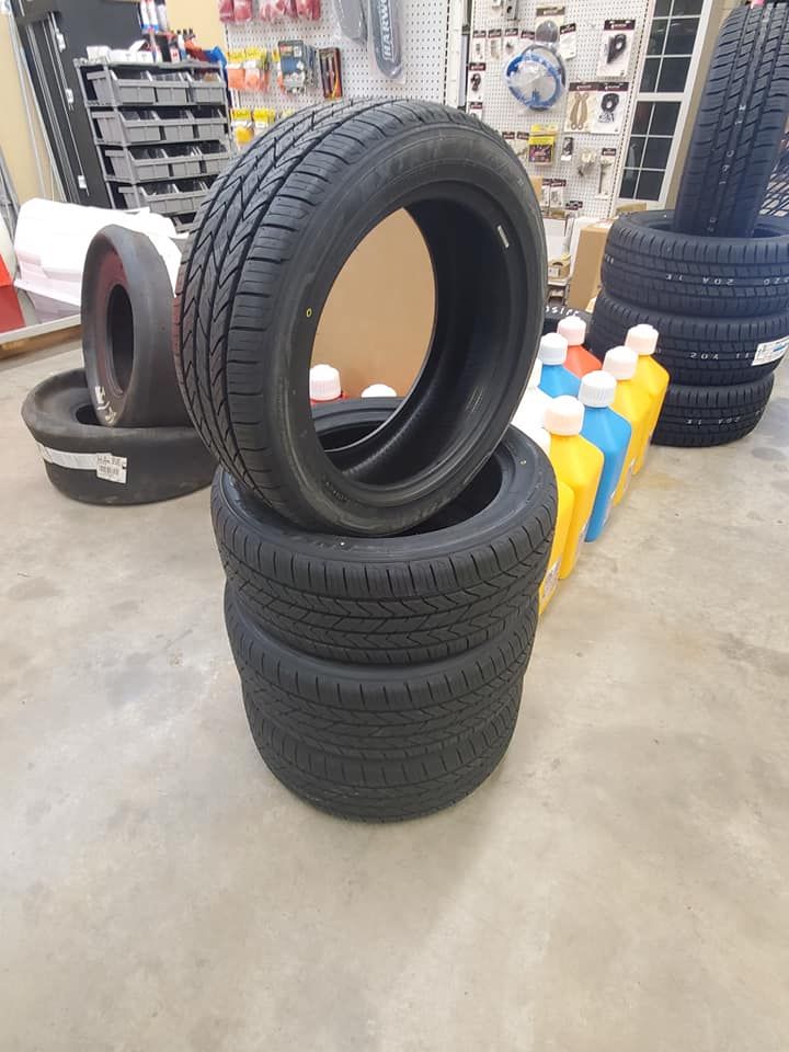 Four black tires stacked; two above, two below. Bottles of oil are nearby.