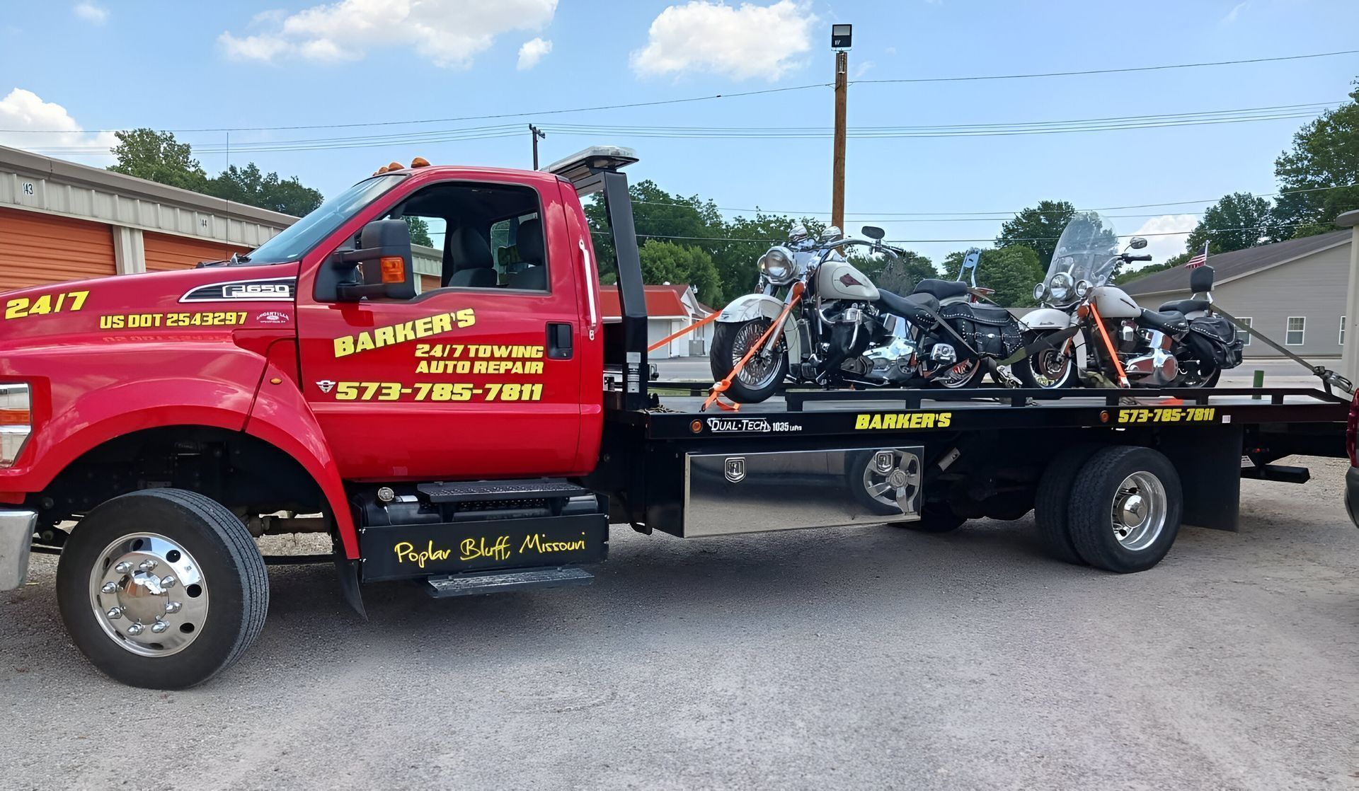 Red tow truck hauling two motorcycles on a sunny day. 