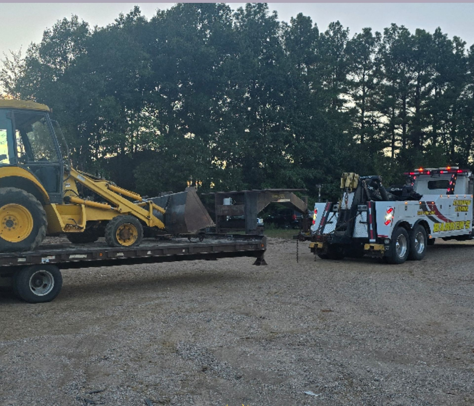 A yellow backhoe on a trailer being towed by a white tow truck.
