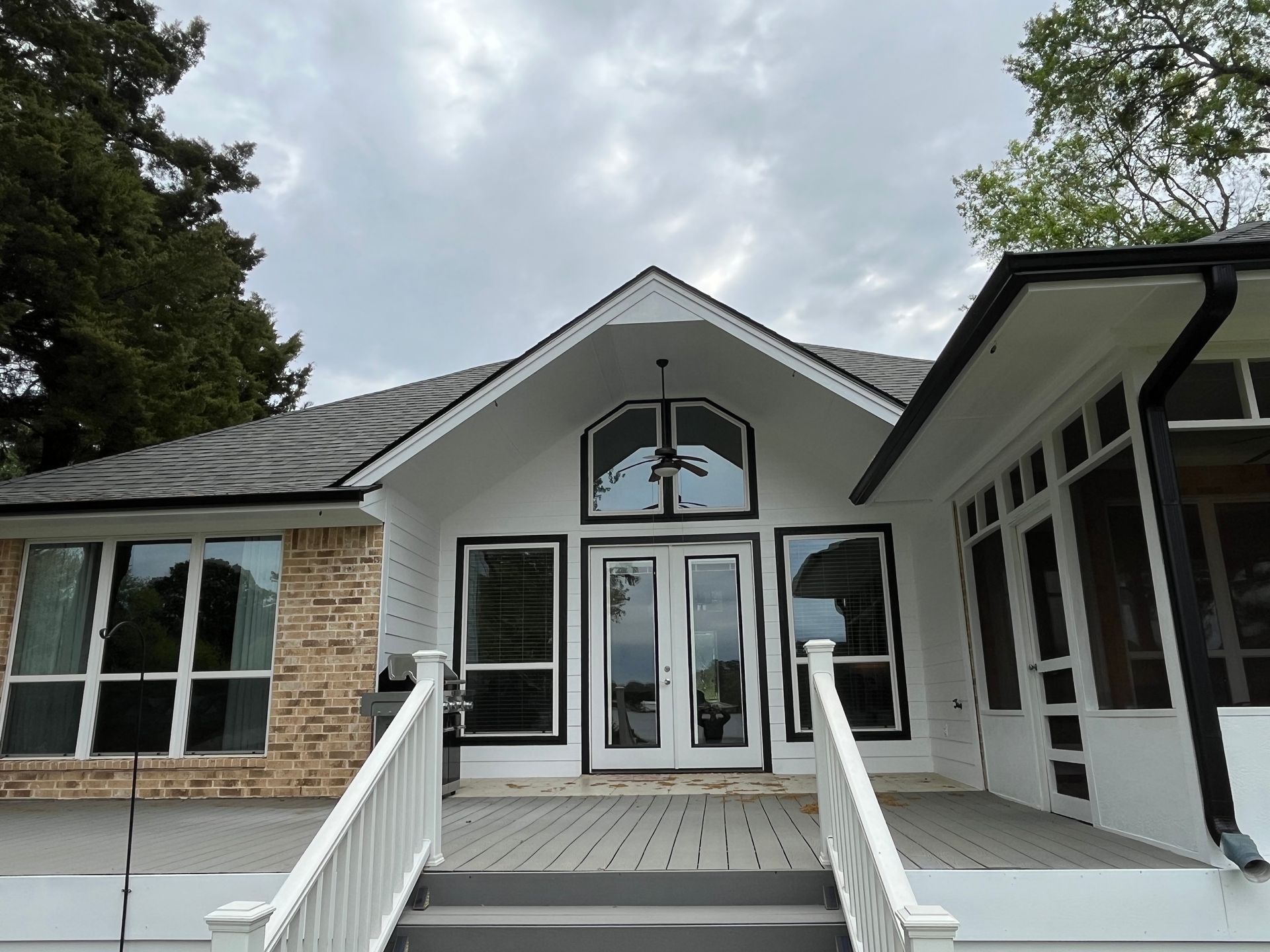 Exterior view of a home with a gray roof, white trim, stone accents, and a deck with stairs and white railings.