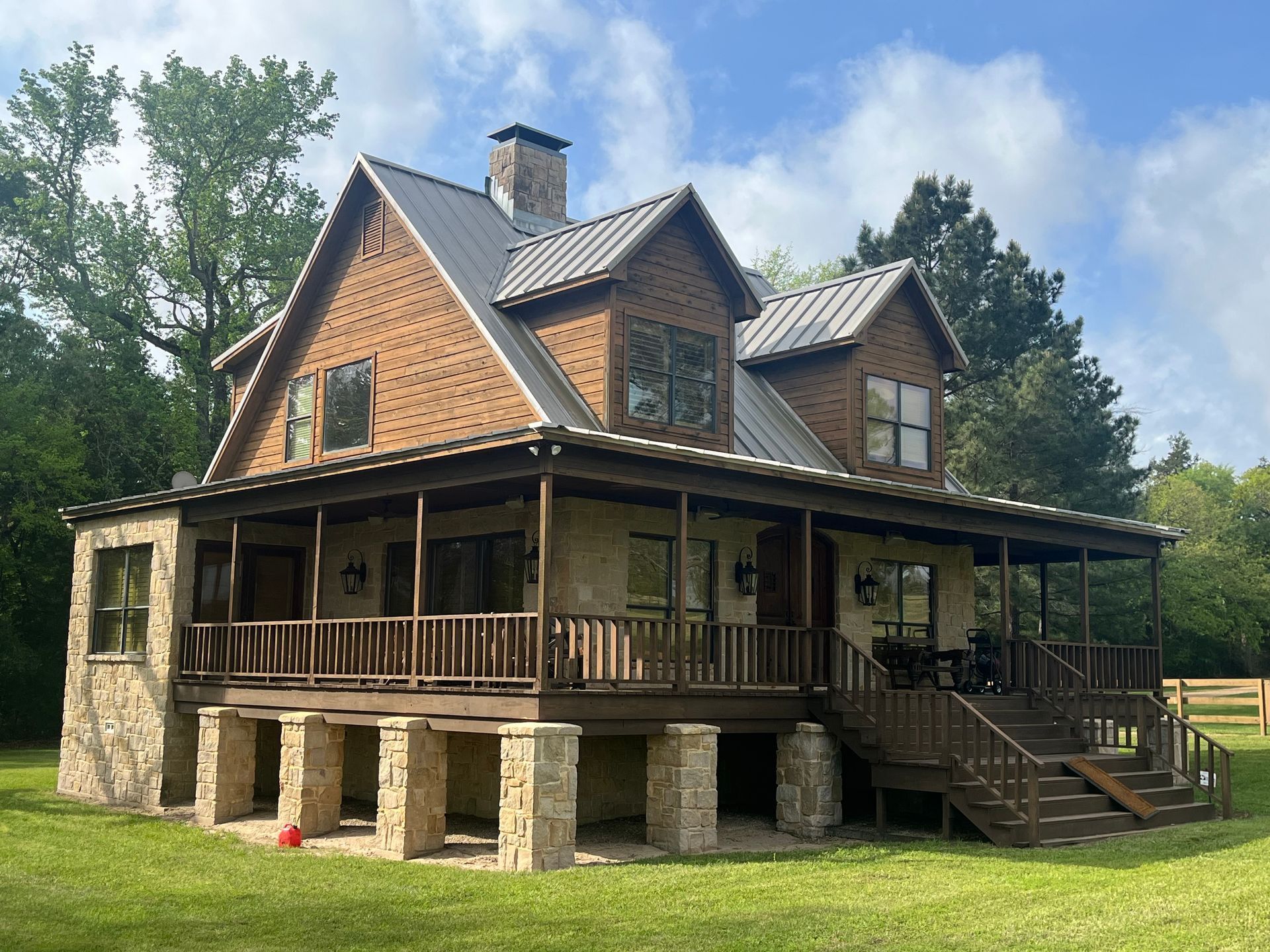 A two-story rustic house with stone siding on the ground floor, wood shingles on the second, and a wide wraparound porch. 