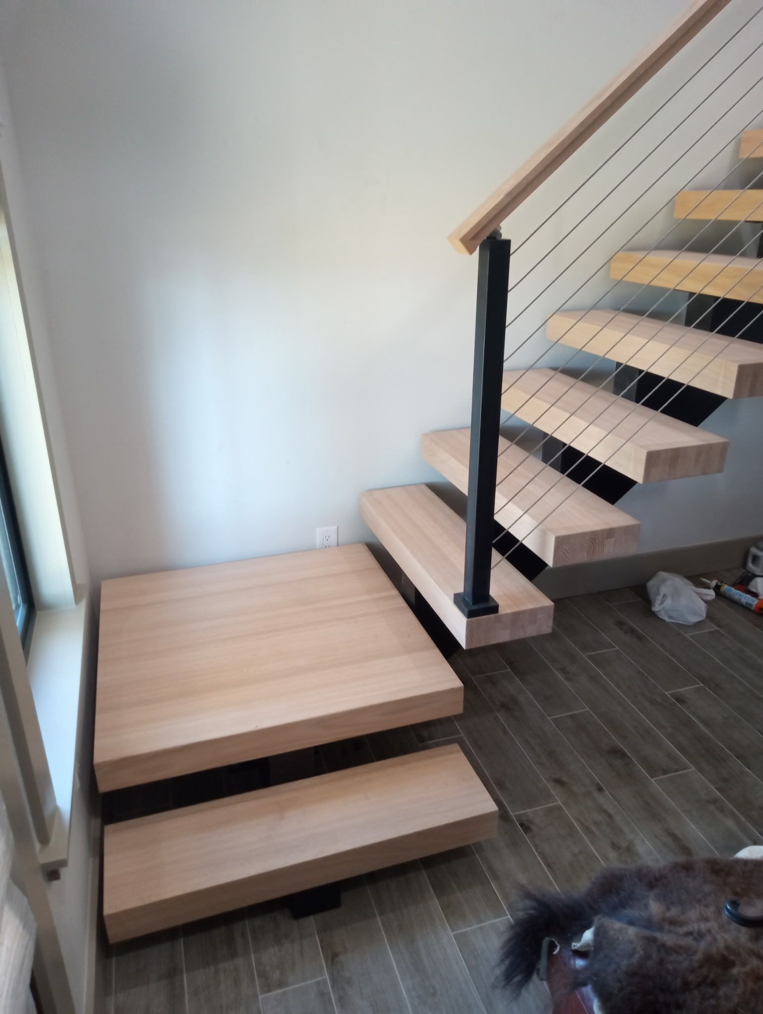Before picture of a wooden staircase with metal accents and cable railing.