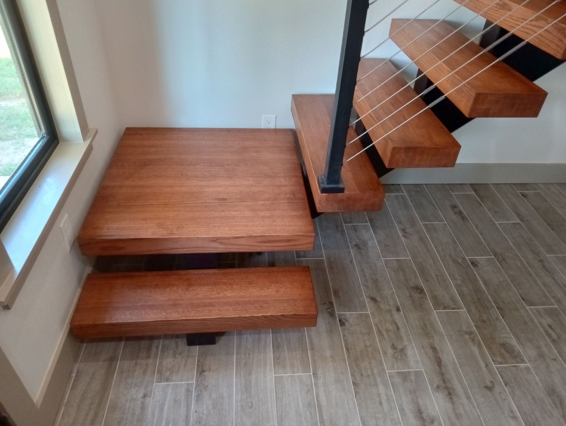 A freshly painted wooden staircase with metal accents and cable railing.