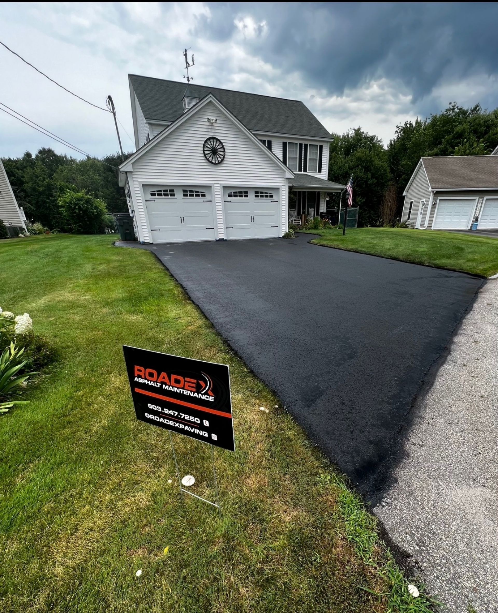 Suburban house with fresh black asphalt driveway and a lawn sign in front